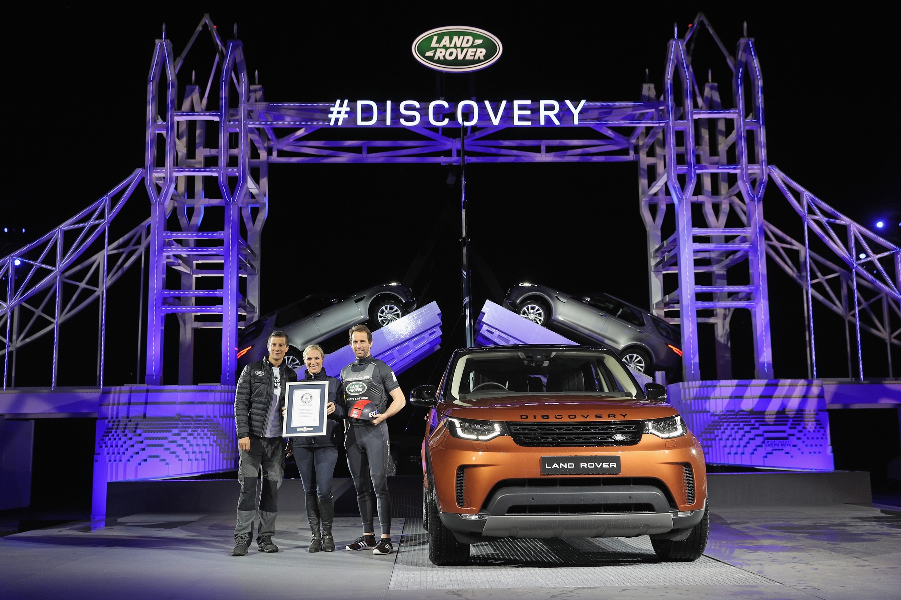 SOLIHULL, ENGLAND - SEPTEMBER 27:  (L-R) Bear Grylls, Zara Phillips and Sir Ben Ainslie pose with a certificate to recognise the official Guinness World Record for the Number of Lego pieces uses in a single structure during the launch of Land Rover's 'New Discovery' at Packington Hall on September 27, 2016 in Solihull, England. Land Rover revealed their brand new Discovery with the help of ambassadors Zara Phillips, Bear Grylls and Sir Ben Ainslie against the backdrop of the replica of London’s Tower Bridge, made entirely from Lego. The structure broke the Guinness World Record for the greatest number of Lego bricks used in a sculpture with over 5.8 million pieces.  (Photo by Dan Kitwood/Getty Images for Land Rover) *** Local Caption *** Bear Grylls